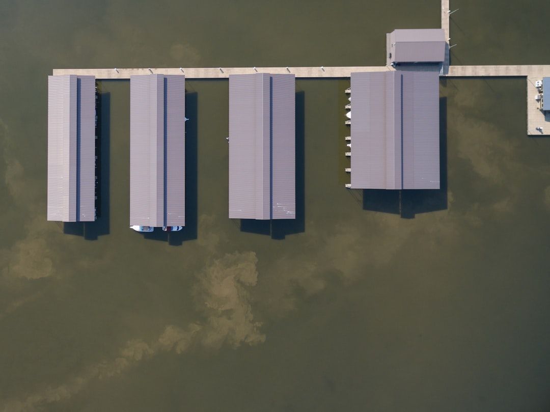 Flygfoto över täckta båtplatser med en brygga som leder till ett mindre hus.